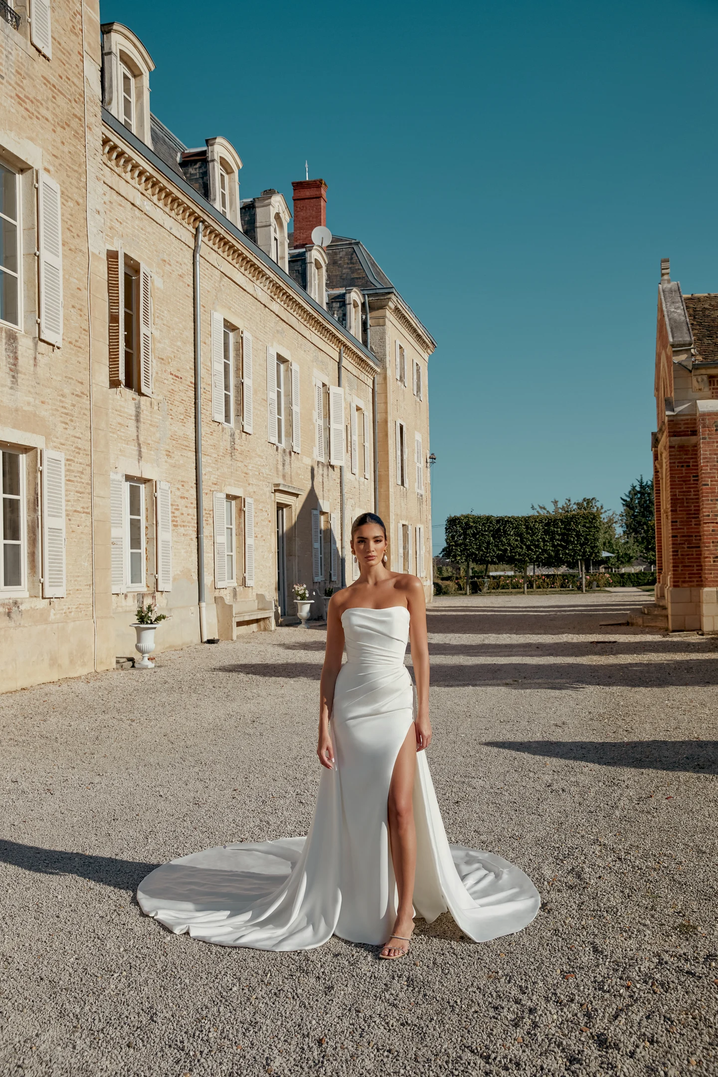 bride standing outside European building in strapless wedding dress with high slit