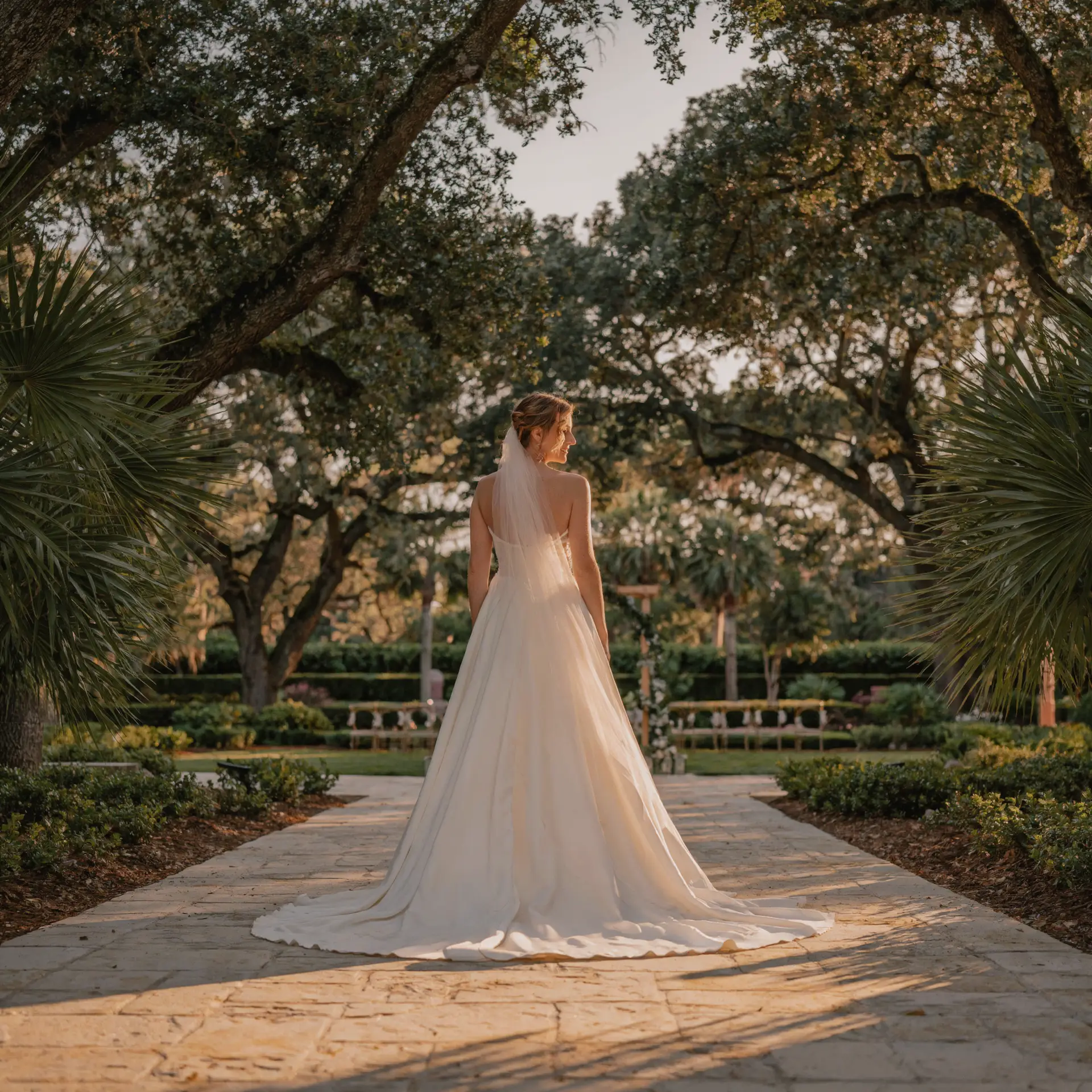 Bride in romantic ivory A-line wedding gown walking down stone aisle at an Orlando area outdoor garden wedding venue at golden hour